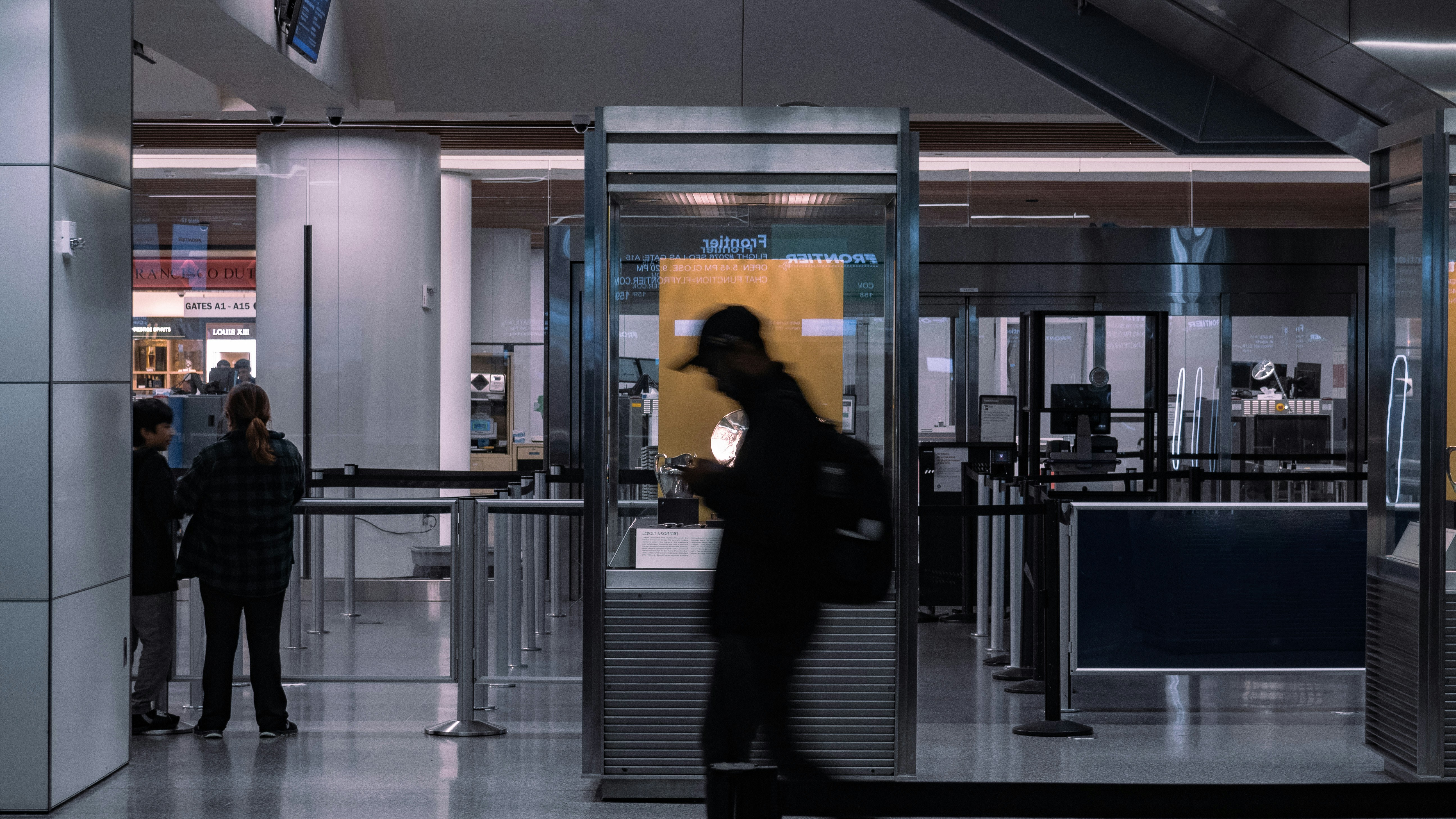 a person walking past quickly, slightly blurred, a security checkpoint at an unspecified airport.