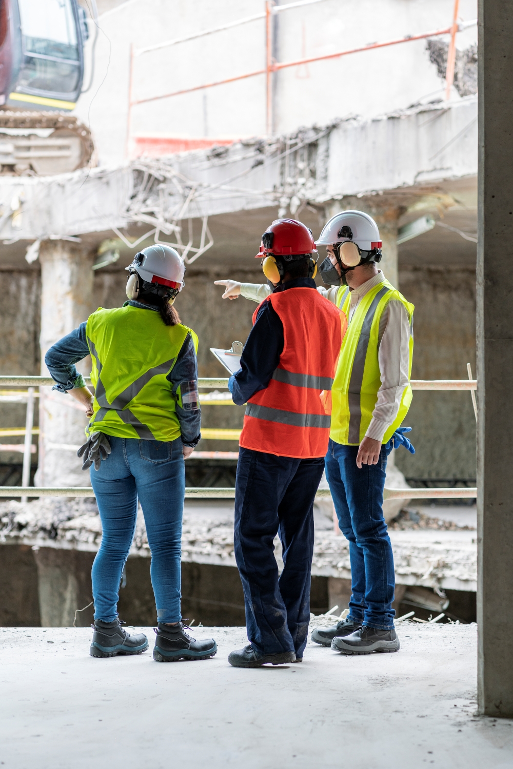 Three construction workers wearing hard hats and reflective safety vests standing inside a partially demolished building.